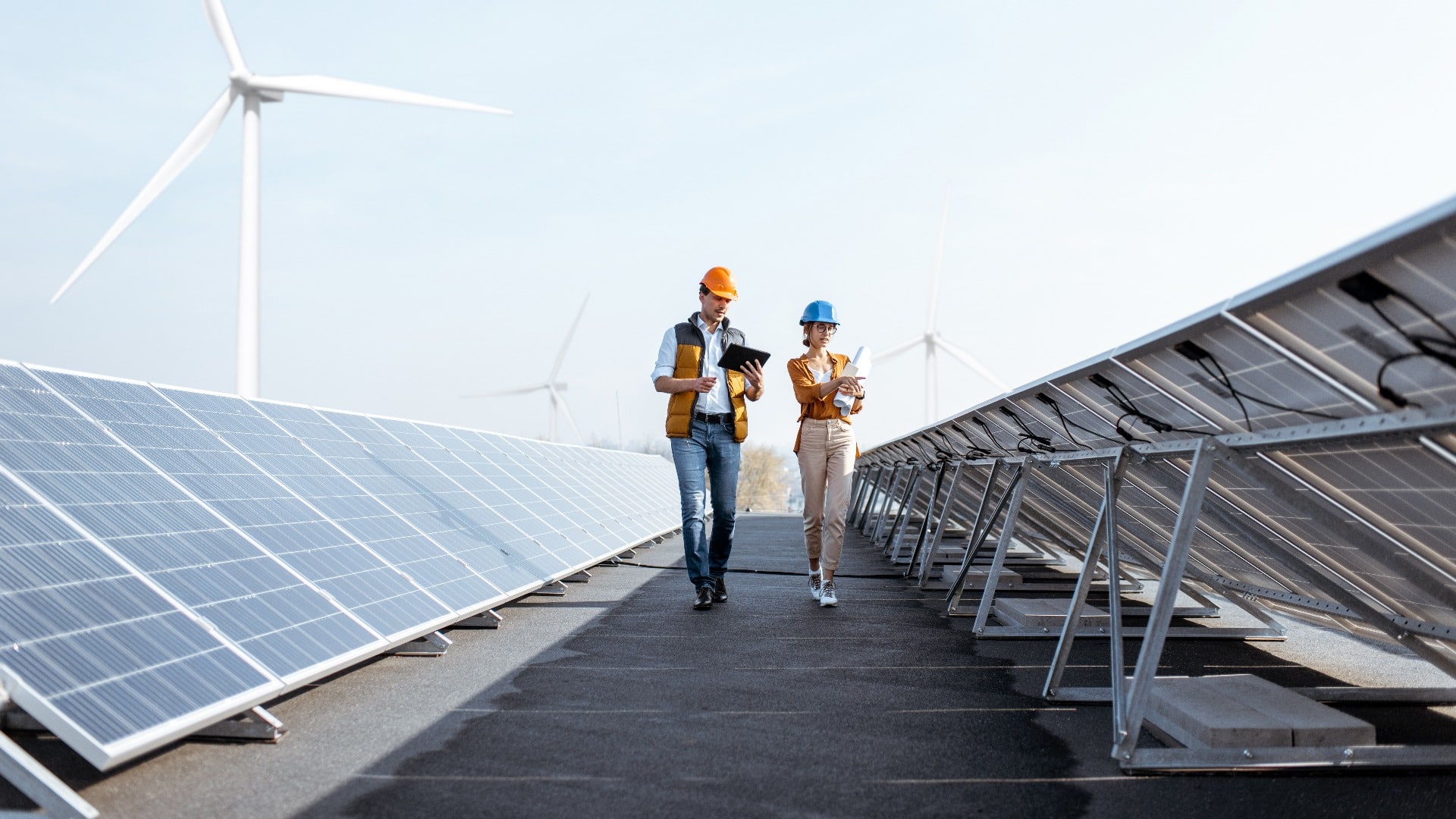 View on the rooftop solar power plant with two engineers walking and examining photovoltaic panels. Concept of alternative energy and its service